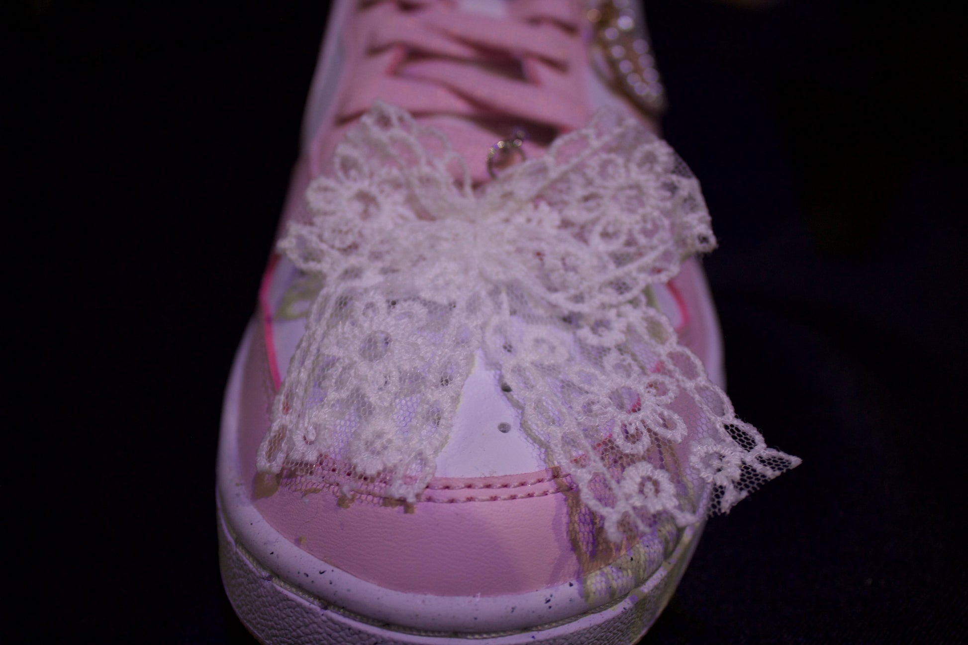 Pink sneaker with a large lace bow on a dark background